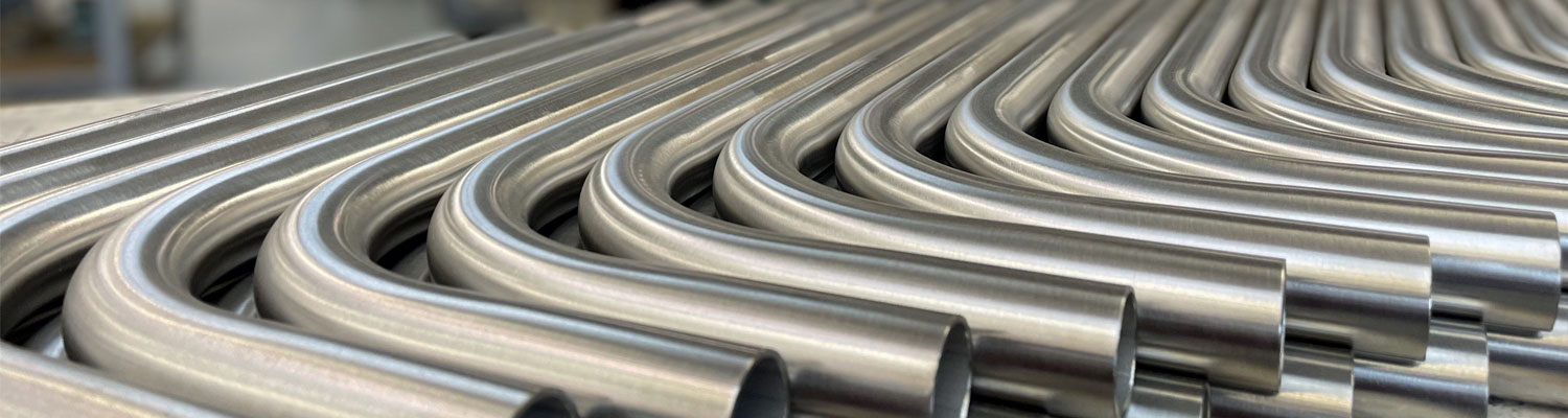 Gebogene Edelstahlrohre mit geschliffener Oberfläche liegen sauber sortiert nebeneinander
