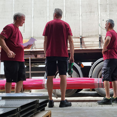 Mitarbeiter-Team in der Werkstatt entlädt Edelstahlrohre von einem LKW und überprüft die Lieferung.