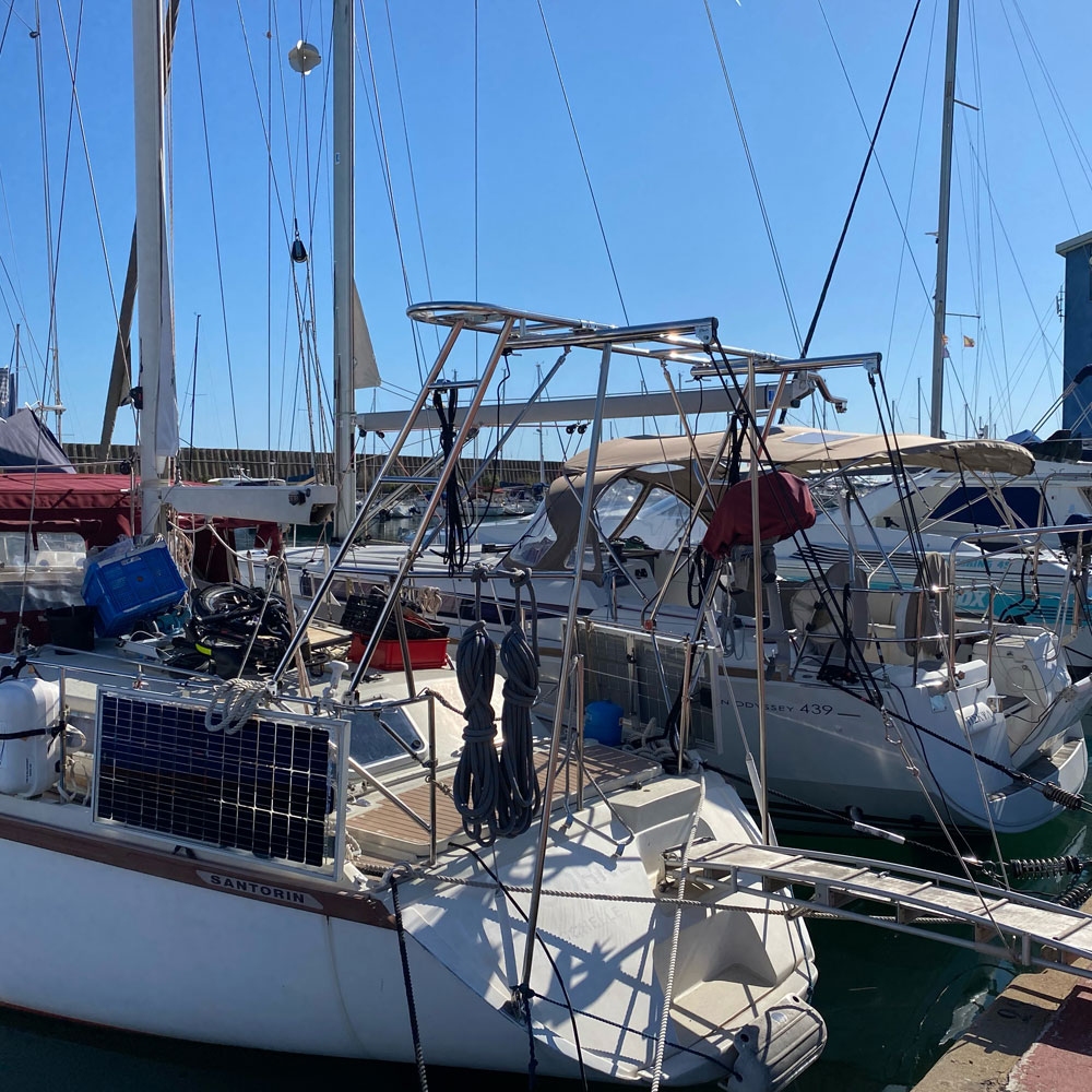 Eine Hafenansicht mit mehreren Segelyachten, die dicht nebeneinander liegen. Im Vordergrund ist eine Yacht mit einem montierten Solarpanel und einem Edelstahl-Davitsystem zu sehen. Weitere Yachten im Hintergrund haben Sonnendächer und diverse Ausrüstungen