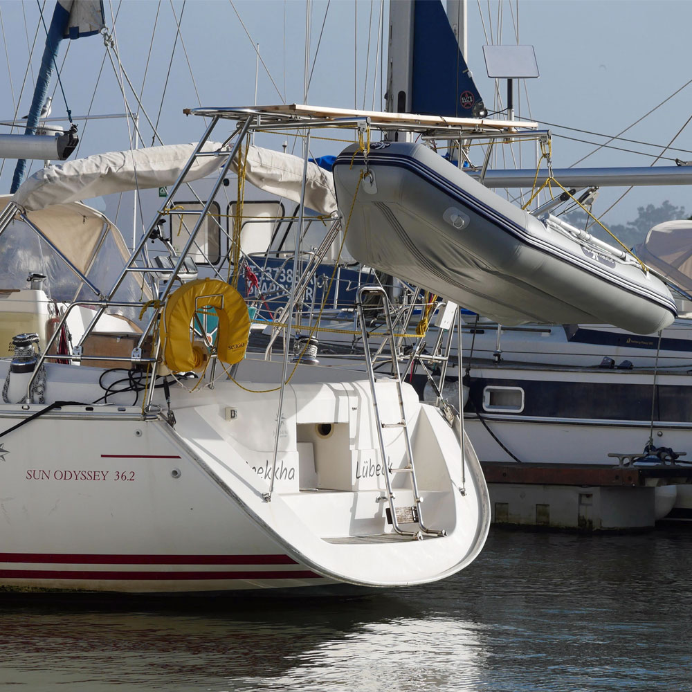 Eine Segelyacht des Modells Sun Odyssey 36.2 liegt im Hafen. Am Heck der Yacht ist ein Edelstahl-Davitsystem montiert, das ein aufgebocktes Beiboot sicher hält. Die Badeplattform und die Badeleiter sind gut sichtbar. Im Hintergrund sind weitere Segelboote