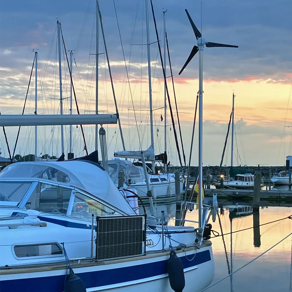 Solarmodul am Heckkorb und Windgenerator am Mast einer Segelyacht in der Marina im Abendlicht – kombinierte Solar- und Windenergie für die netzunabhängige Stromversorgung an Bord beim Törn auf der Ostsee.